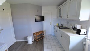 A compact kitchen with white cabinets, a sink, a toaster, and a television on the wall. - Söl'ring Hüs SO/19 - Söl'ring Hüs (Sylt)
