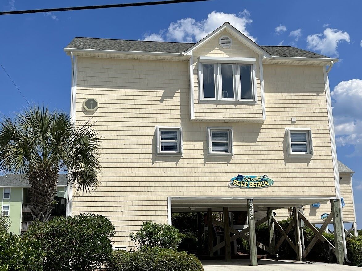 A two-story building with a garage entrance, a sign reading "Naresville Surf Shack," and a palm tree in the foreground.