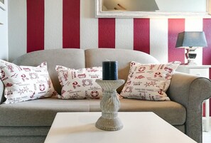 Ein Wohnzimmer mit einer Couch, gemusterten Kissen, einem Deko-Kerzenhalter und einer gestreiften Wand.