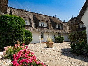 A traditional thatched-roof house with a stone courtyard, surrounded by well-maintained hedges and flowering plants. - Söl`ring Hüs "Nautica" SO/22 - Söl'ring Hüs (Sylt)