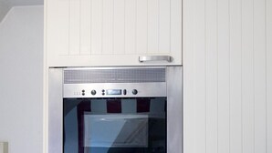 Una cocina con horno empotrado, campana extractora de acero inoxidable y repisa de vidrio sobre el horno.