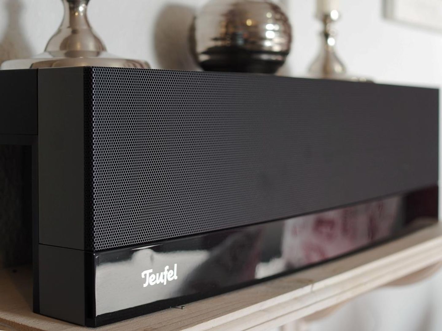 A black Teufel speaker on a wooden shelf.