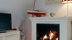 Una habitación con una chimenea blanca, un televisor sobre un mueble y una silla roja colgada en la pared.