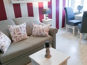 A living room with a sofa, two pillows, a table with a candle, a lamp, and a chair. - Söl`ring Hüs "Nautica" SO/22 - Söl'ring Hüs (Sylt)