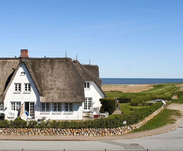 Et hus med stråtækt tag og hvid facade, en stenvæg og havudsigt.