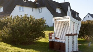 A beach chair with a striped canopy and a cushion, placed on grass in front of a house with a thatched roof. - Söl`ring Hüs S0/29 - Söl'ring Hüs (Sylt)