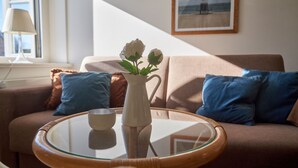 A living room with a sofa, cushions, a glass coffee table, a white vase with flowers, and a framed picture on the wall. - Söl`ring Hüs S0/29 - Söl'ring Hüs (Sylt)