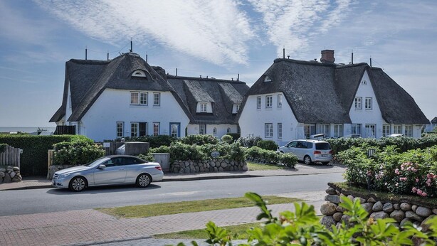 A row of white houses with thatched roofs, a paved driveway, and parked cars. - Söl`ring Hüs "Rantumer Perle" App. SO/01 - Söl'ring Hüs (Sylt)