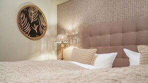 A neatly made bed with white and striped pillows, a round wall art piece, and a textured wall behind the bed. - Söl`ring Hüs "Rantumer Perle" App. SO/01 - Söl'ring Hüs (Sylt)