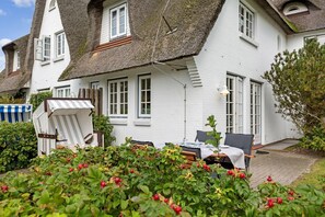 A white house with a thatched roof, a dining area with a table and chairs, and a garden with strawberries. - SO/10 Söl`ring Hüs Raantem Lek - Söl'ring Hüs (Sylt)