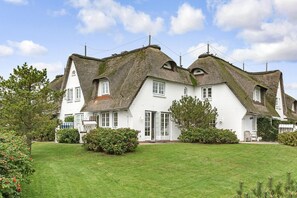 Une maison blanche avec un toit de chaume et une pelouse bien entretenue.