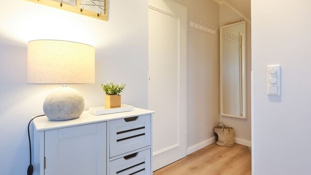 A hallway with a white cabinet, a lamp, a small plant, a coat rack, a mirror, and a door. - SO/10 Söl`ring Hüs Raantem Lek - Söl'ring Hüs (Sylt)