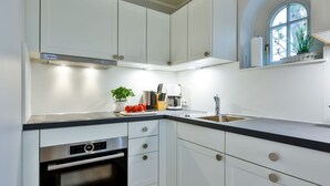 A modern kitchen with white cabinetry, a built-in oven, a coffee maker, and a window with a view of greenery. - SO/10 Söl`ring Hüs Raantem Lek - Söl'ring Hüs (Sylt)