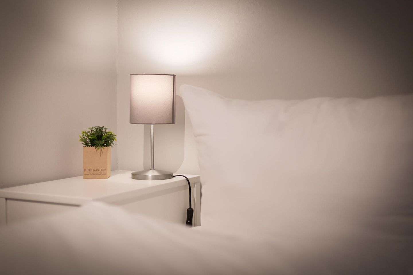 A bedside table with a lamp, a small plant, and a power cord.