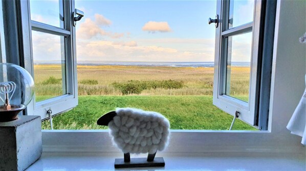A window with an open view of a grassy field and a sheep figurine on a stand. - Söl`ring Hüs "Wattkieker" SO/23 - Söl'ring Hüs (Sylt)