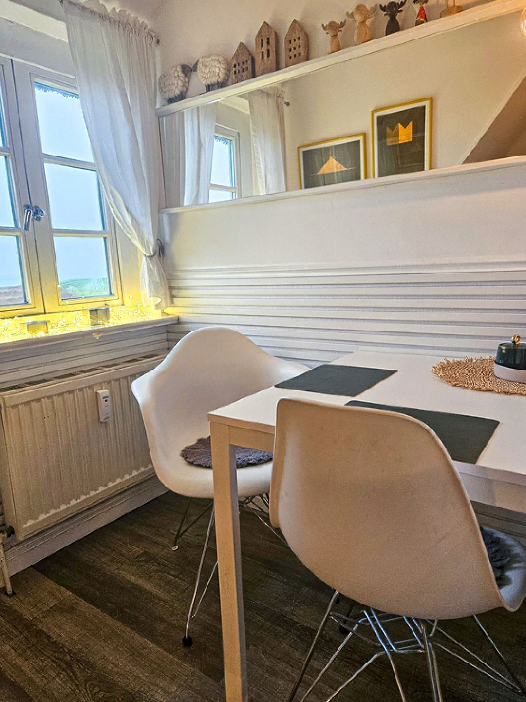 Eine moderne Küche mit weißer Arbeitsplatte, zwei weißen Stühlen, einem Fenster mit Vorhängen und einem Regal mit Dekoration.