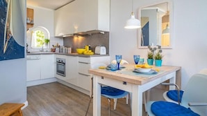 A modern kitchen with white cabinets, a wooden countertop, and blue chairs. - Söl`ring Hüs "Meerblick" SO/06 - Söl'ring Hüs (Sylt)