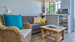 A cozy living room with a wicker sofa, a grey couch, a wooden coffee table, and a bookshelf. - Söl`ring Hüs "Meerblick" SO/06 - Söl'ring Hüs (Sylt)