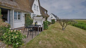 Une rangée de maisons blanches aux toits de chaume, une terrasse avec une table et des chaises, et un petit arbre au premier plan.