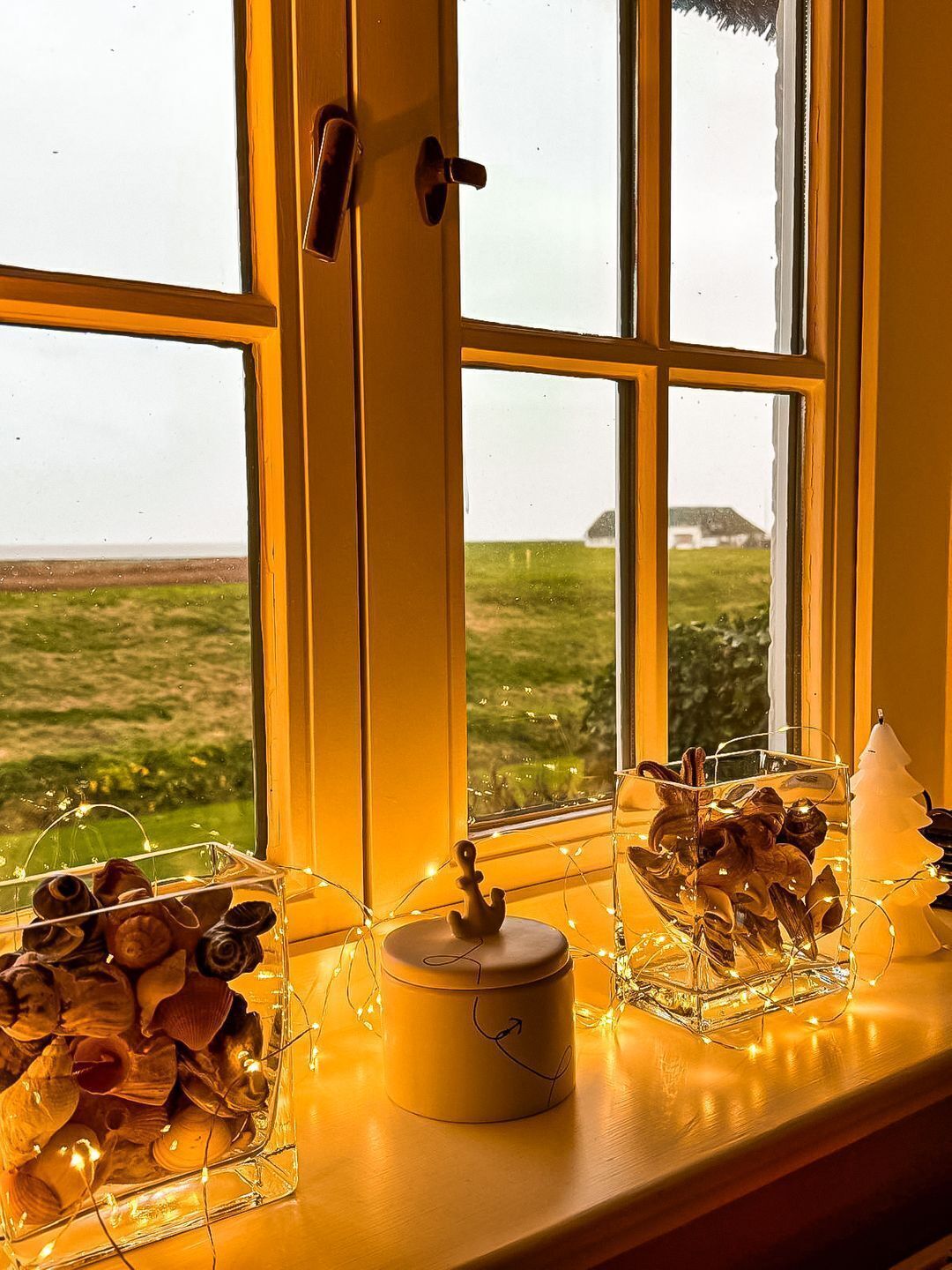 Une fenêtre donnant sur un paysage rural, une porte et une étagère ornée d’objets décoratifs et de luminaires.