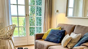 Un salon comprenant un canapé, une table basse en verre, un pouf rond et un fauteuil.