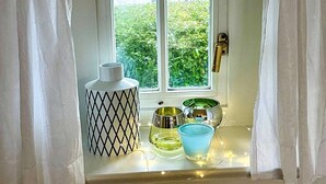 Une fenêtre donnant sur un paysage verdoyant, une porte blanche et une petite étagère ornée d’objets décoratifs.