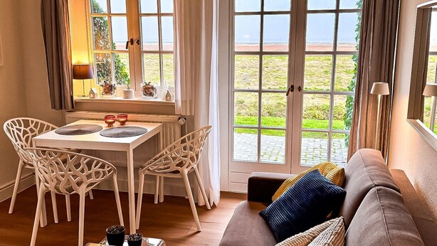 Un salon chaleureux avec un canapé, une table à manger et des chaises, et de grandes fenêtres donnant sur la plage.