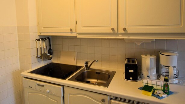 A kitchen with white cabinets, a double sink, a dishwasher, and a coffee maker.