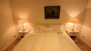 A neatly made bed with white linens, two bedside tables with lamps, and a framed painting on the wall. - Söl'ring Hüs app. SO/15 - Söl'ring Hüs (Sylt)