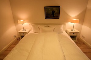 Un lit bien fait, avec du linge de lit blanc, deux tables de chevet avec des lampes et un tableau encadré au mur.