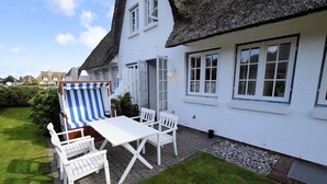 A white house with a thatched roof, a patio with a table and chairs, and a striped beach chair. - Söl'ring Hüs app. SO/15 - Söl'ring Hüs (Sylt)