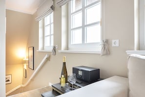 Habitación de hotel con una escalera, un minibar, una botella de vino y una copa de vino sobre una mesita.