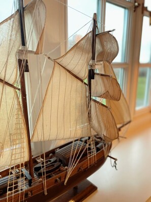 Une maquette de bateau très détaillée, avec des cordages et des voiles apparents, exposée à l’intérieur, avec une fenêtre en arrière-plan.