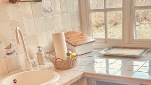 Une cuisine avec un évier blanc, des placards en bois, un égouttoir et une fenêtre donnant sur des arbres.