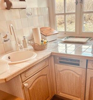 A kitchen with a white sink, wooden cabinets, a dish rack, and a window with a view of trees. - Hellas Hüs - Hellas Hüs ST/48 (Sylt)