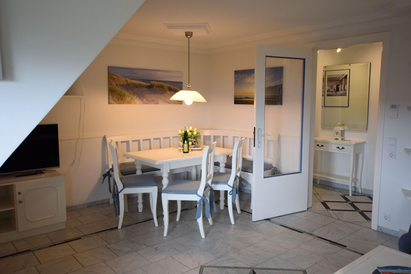 A dining area with a white table and chairs, a television on a stand, and artwork on the walls.