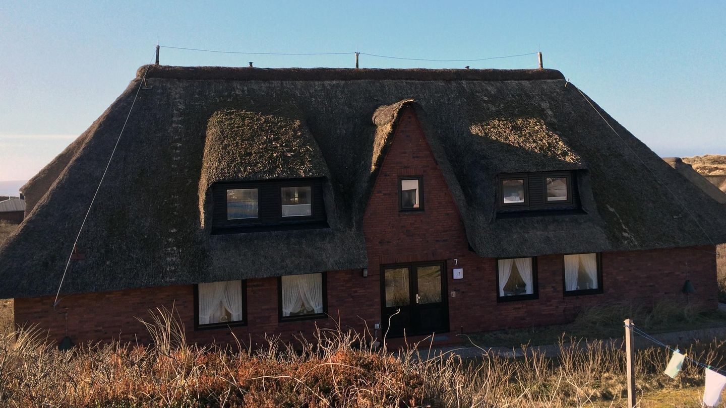 Une maison traditionnelle à toit de chaume, avec une partie inférieure en briques, portant le numéro 7, et une petite porte d’entrée.
