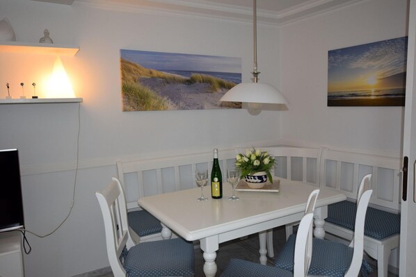 A dining area with a white table, blue cushioned chairs, a white pendant light, and two framed landscape paintings. - Strandstraße 26 - ST/26 Im Dünen Wai 07 (Sylt)