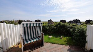 A beachside garden with a striped beach chair, a white fence, and houses in the background. - House Wattblick App. 02 - Wattblick (Sylt)
