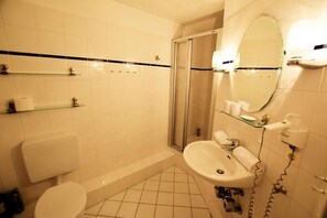Ein Badezimmer mit Toilette, Waschbecken, Dusche und einer Glasablage mit Pflegeprodukten.