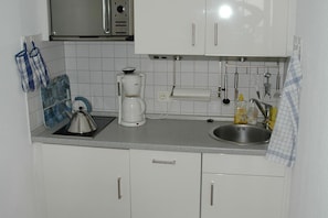 A compact kitchen with white cabinets, a stainless steel sink, a kettle, a coffee maker, and a microwave. - House Wattblick App. 03 - Wattblick (Sylt)