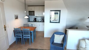 Een compacte keuken met witte kastjes, een eettafel met blauwe stoelen en een kitchenette.