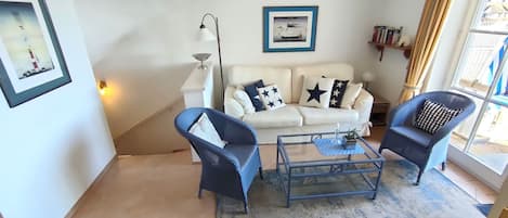 A living room with a white sofa, two blue armchairs, a glass coffee table, and a floor lamp.
