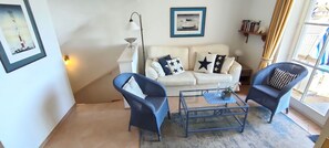 A living room with a white sofa, two blue armchairs, a glass coffee table, and a floor lamp. - House Wattblick App. 03 - Wattblick (Sylt)