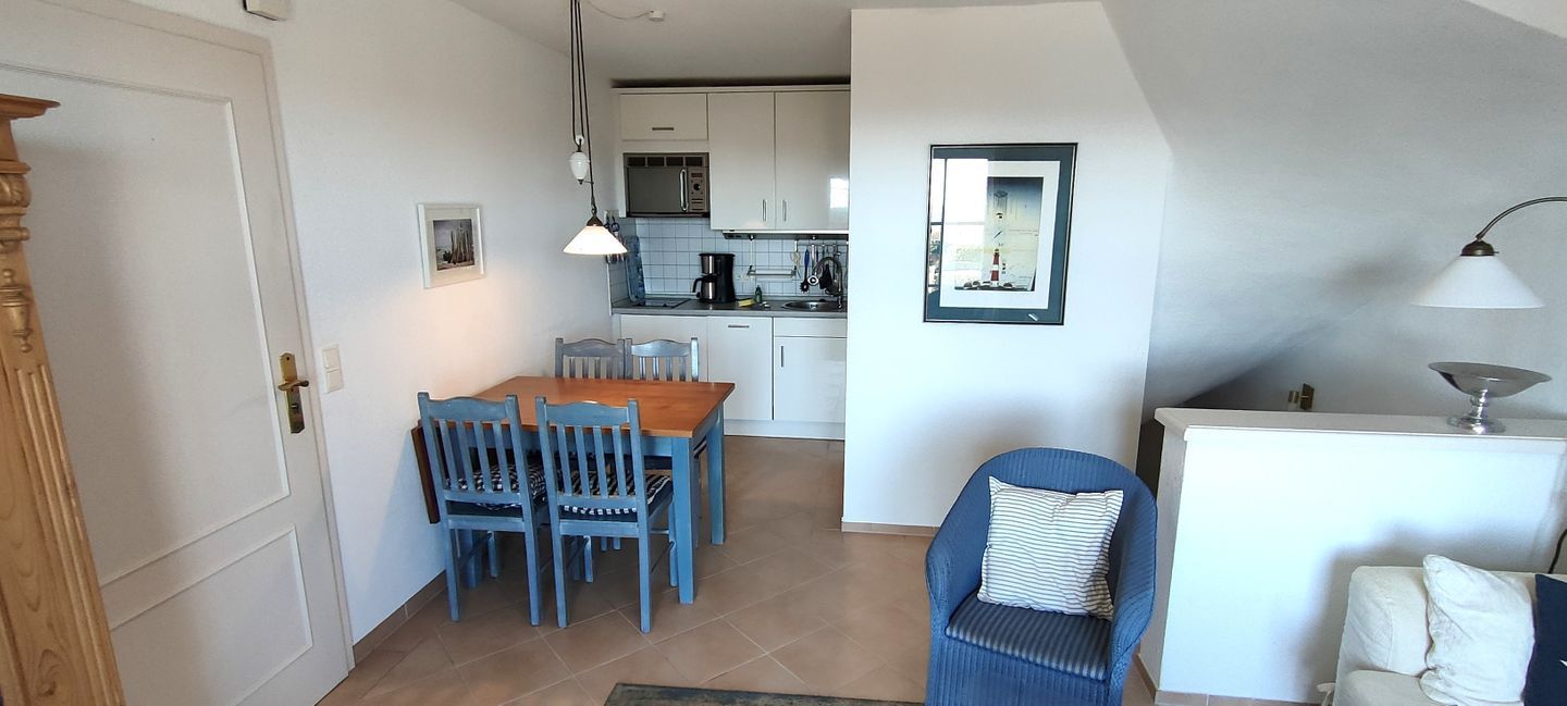 A compact kitchen with white cabinets, a dining table with blue chairs, and a kitchenette area.