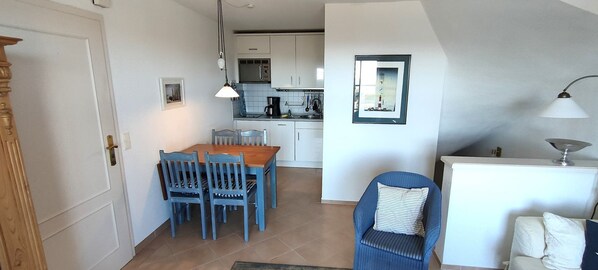 Une cuisine compacte avec des meubles blancs, une table à manger avec des chaises bleues et un coin cuisine.
