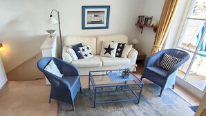 Een woonkamer met een witte bank, twee blauwe fauteuils, een glazen salontafel en een vloerlamp.