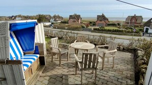 A patio with wicker furniture, a round table, and chairs. - House Wattblick App. 03 - Wattblick (Sylt)
