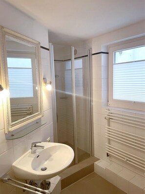 A bathroom with a glass-enclosed shower, a white sink, and two wall-mounted mirrors.