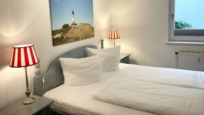 Ein Schlafzimmer mit einem Bett, zwei Nachttischlampen, einem Gemälde eines Leuchtturms und einem Fenster mit Blick.